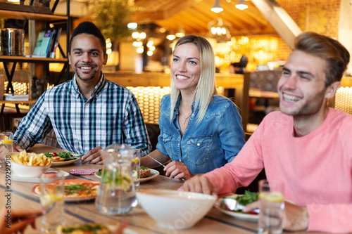 Group of young multi-ethnic friends having dinner at cafe, talking and laughing