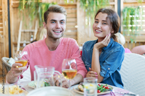 Happy young couple smiling at camera while having dinner in restaurant  handsome man wearing dental braces