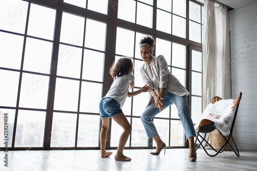 Happy loving afro american family. Young mother and her daughter playing in the nursery. Mom and daughter are dancing on the background of a large window