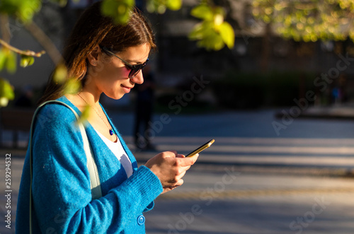 Side portrait of a young woman wearing sunglasses checking her phone
