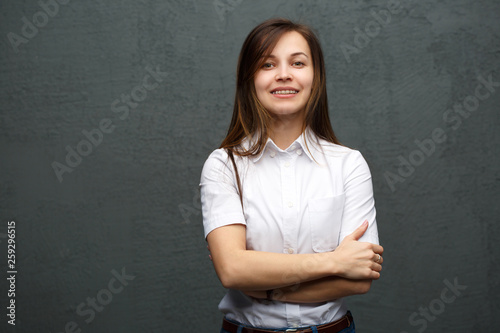 Portrait of a smiling girl with brekits in strict casual clothing with disheveled hair against a gray wall.