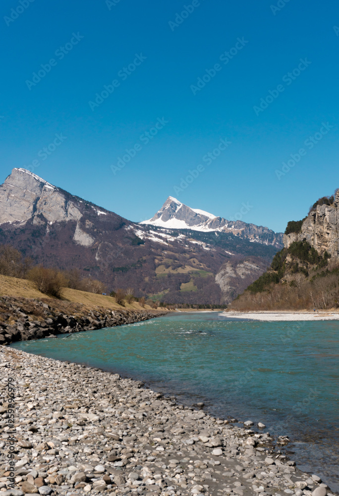 clear wide mountain river with snow-capped peaks behind under a clear blue sky