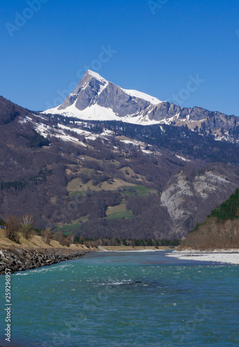 clear wide mountain river with snow-capped peaks behind under a clear blue sky photo
