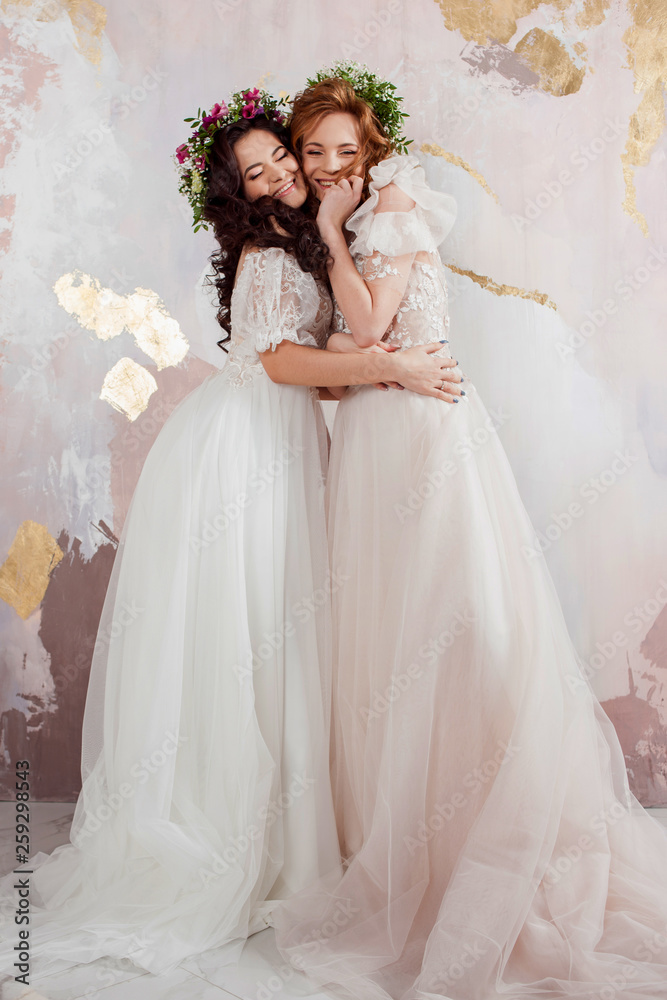 Two charming brides in beautiful spring wreaths on their heads. Beautiful young women in wedding dresses Two charming brides in beautiful spring wreaths on their heads. Beautiful young women in wedding dresses
