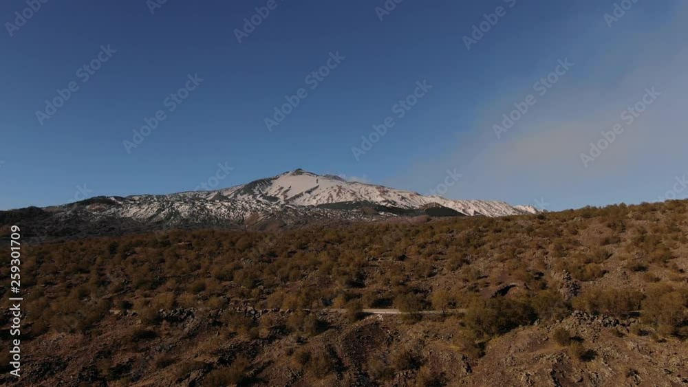 Aerial descending view over of the summit of mount Etna in Sicily (Italy) with lava rock and shrubs in the foreground Aerial descending view over of the summit of mount Etna in Sicily (Italy) with lava rock and shrubs in the foreground