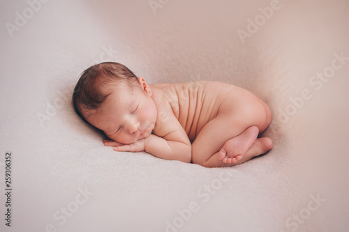 naked newborn baby sleeping curled up in a ball