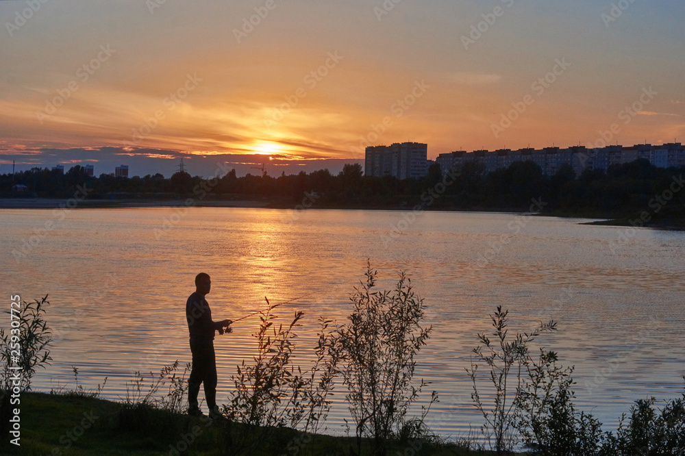 Fototapeta premium Angler on the river Bank against the sunset sky.