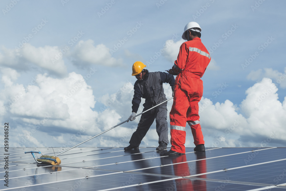 technician operating and cleaning solar panels at generating power of solar power plant; technician in industry uniform on level of job description at industrial technician operating and cleaning solar panels at generating power of solar power plant; technician in industry uniform on level of job description at industrial