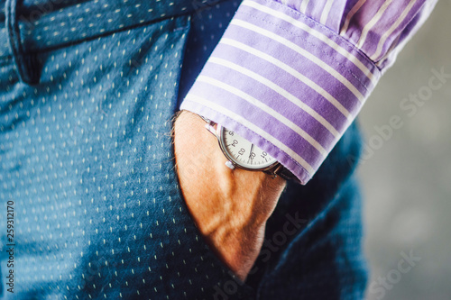 Close-up of Male Hand in Pants Pocket with Elegant Wristwatch. Caucasian Businessman in Striped Shirt Wearing Stylish Dress Watch. Fashion and Punctuality Concept