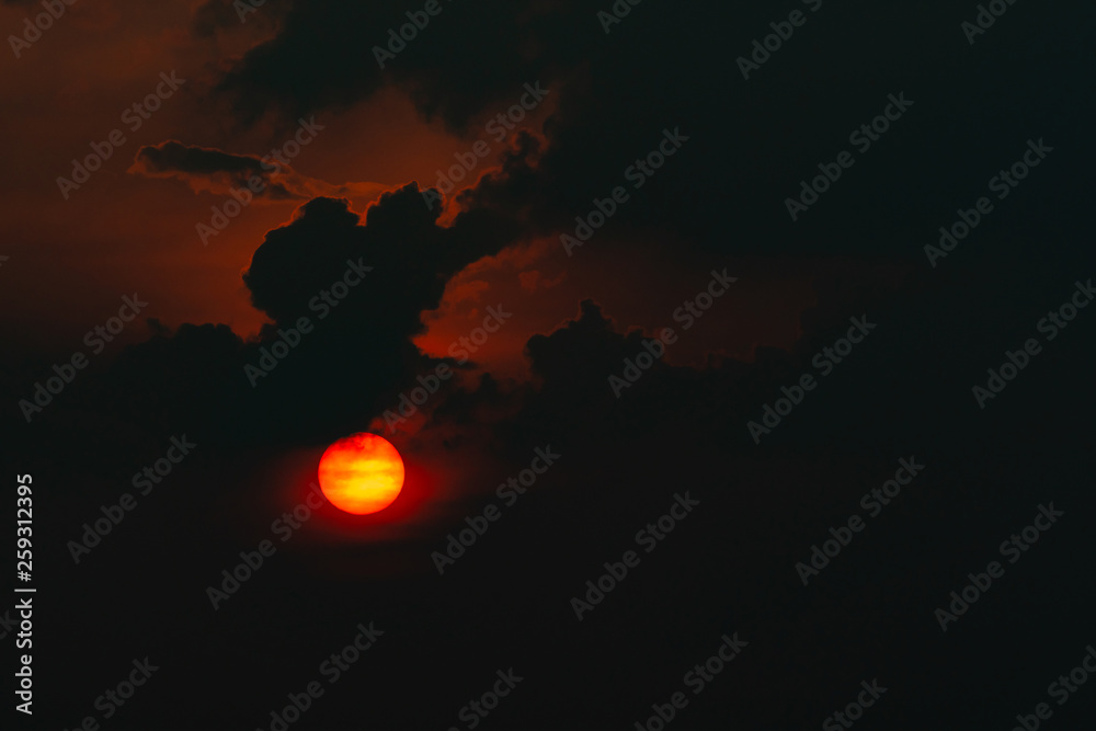 Red big sun in dark clouds. Devil sunset. Horror view of sun in black clouds sky. Summer sunset. Fiery sun in the evening. Nature background. Dramatic sky with big sun. Heat weather. Heaven concept.