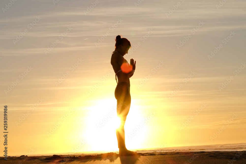 An awesome yoga instructor does some poses on the beach with the sunrise