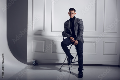 Φωτογραφία Portrait of a handsome, attractive, sexy, confident, elegantly men in black-gray suit and glasses, sitting on chair, posing in studio isolated on white background