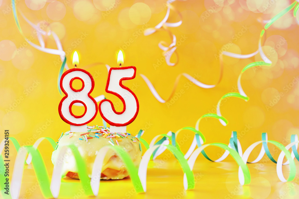 Eighty five years birthday. Cupcake with burning candles in the form of number 85. Bright yellow background with copy space