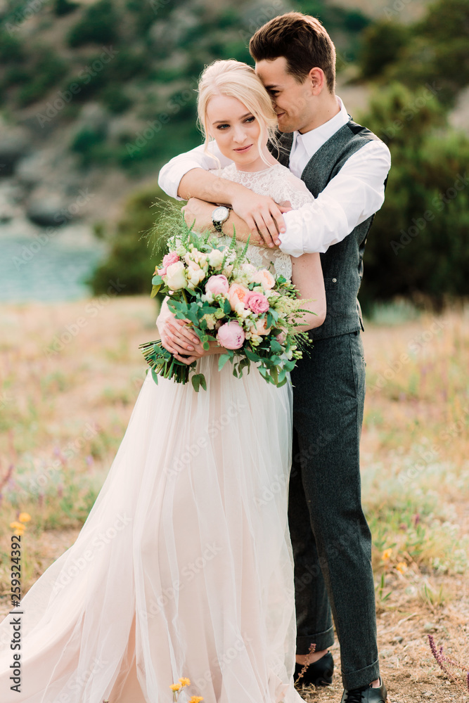Stunning bride and groom hug each other tender standing on the golden hill Stunning bride and groom hug each other tender standing on the golden hill