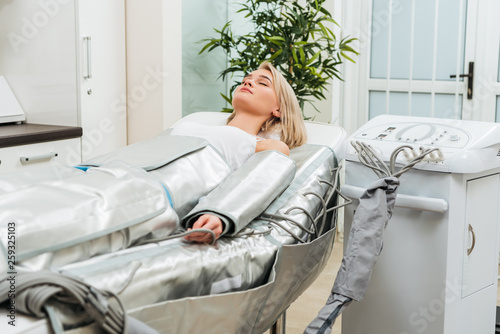 Blonde girl lying with closed eyes during pressotherapy session in clinic