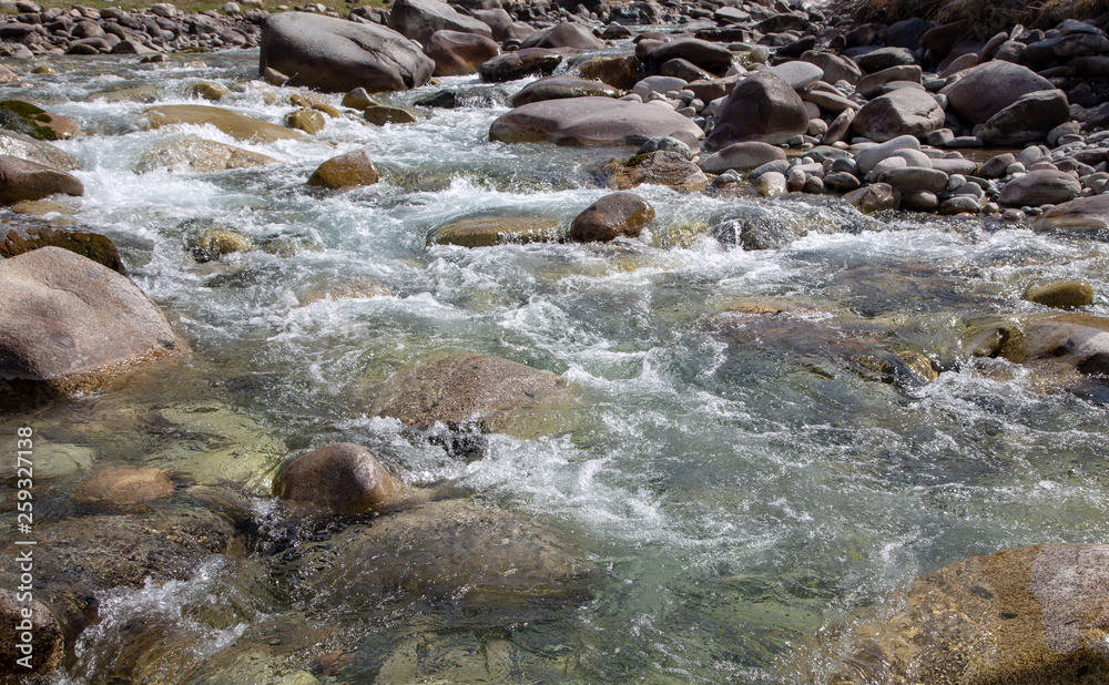 Obraz premium Water in the mountain raging river. Beautiful natural background of stones and water. Texture of clear water and fast river. Background to insert text. Tourism and travel.