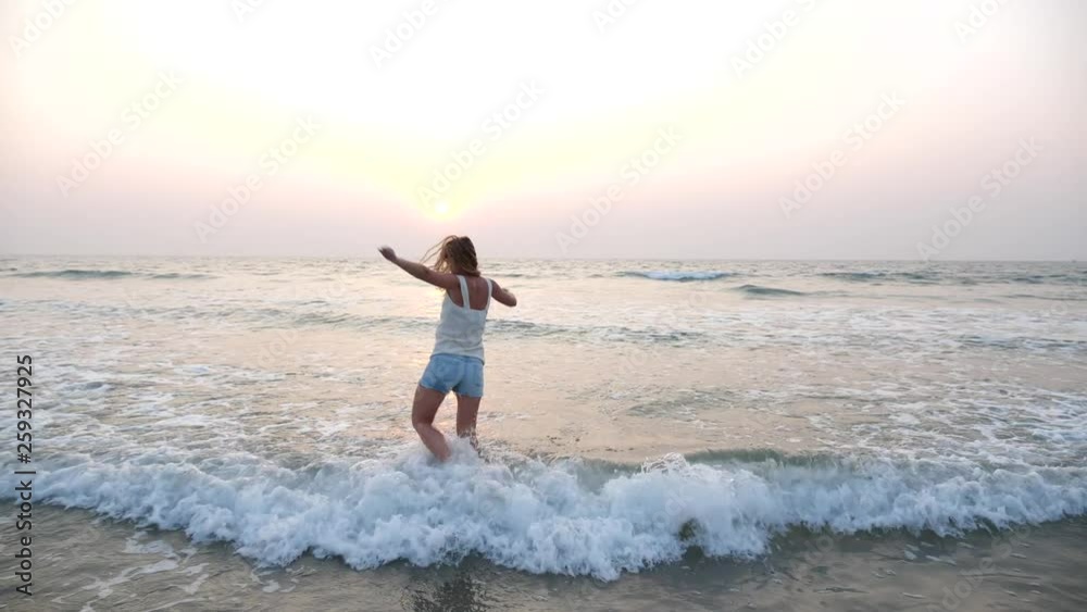A young slim longhaired girl in sunglasses dances in the sea at sunset and splashes fly from the waves. Happy woman resting on the sea on vacation. A young slim longhaired girl in sunglasses dances in the sea at sunset and splashes fly from the waves. Happy woman resting on the sea on vacation.