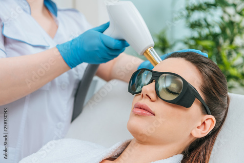 Relaxed woman in protective goggles receiving laser treatment in clinic