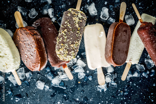 Assortment of various popsicle ice cream, vanilla and chocolate, with nuts, on a dark concrete background with ice, copy space top view