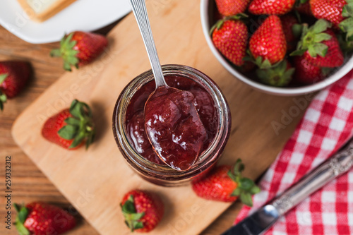 Jar of strawberry jam on wooden background from top view