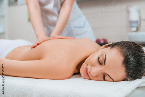 Partial view of masseur doing back massage to girl on massage table