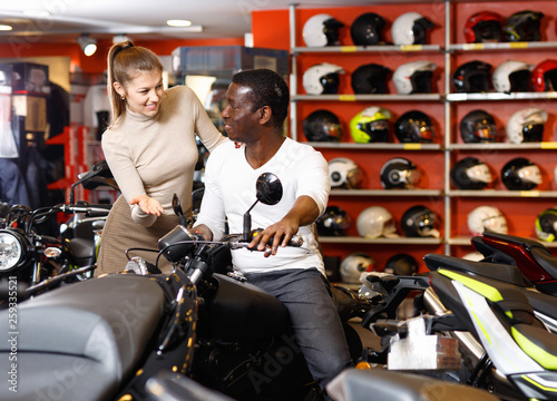 Happy young couple choosing and buying new motorcycle in moto salon