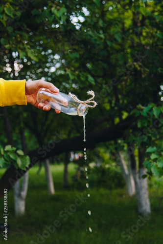 male hand pours homemade lemonade from a bottle on a background of trees on the nature outdoors. close-up, healthy food, diet, proper nutrition, picnic. Summer.