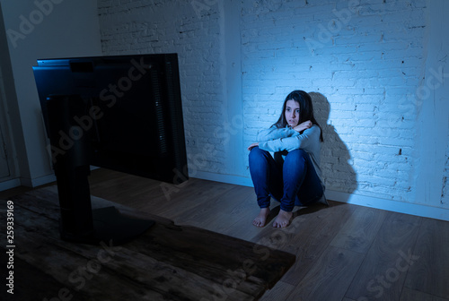 Portrait of young depressed woman sitting on the floor staring a computer suffering cyberbullying