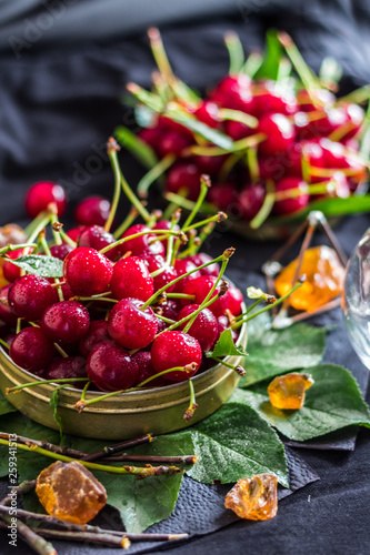 A handful of ripe red cherries in a metal can on a black background with green leaves
