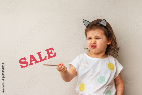 Photography A little girl with pouting lips and provoking emotion points to the words Sale,