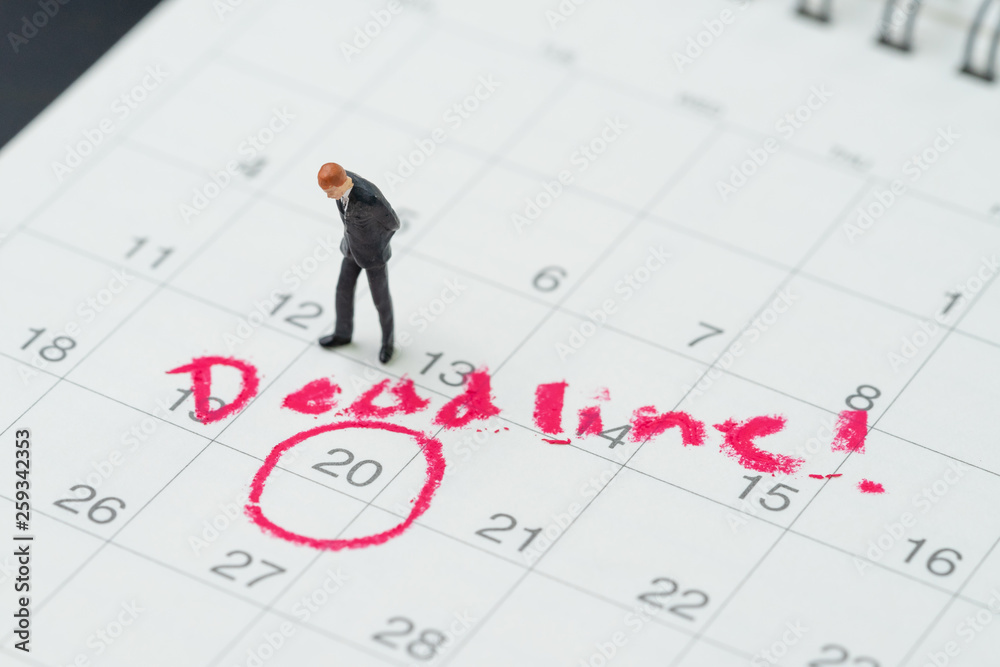 Miniature business man standing on desktop calendar with red circle on important date with handwriting deadline, goal or target date of work project plan, meeting or day of delivery Miniature business man standing on desktop calendar with red circle on important date with handwriting deadline, goal or target date of work project plan, meeting or day of delivery