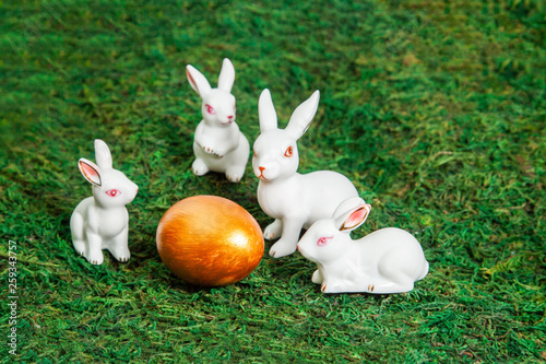 Happy Easter. Congratulatory easter background. Little white bunnies around golden egg on a background of moss.