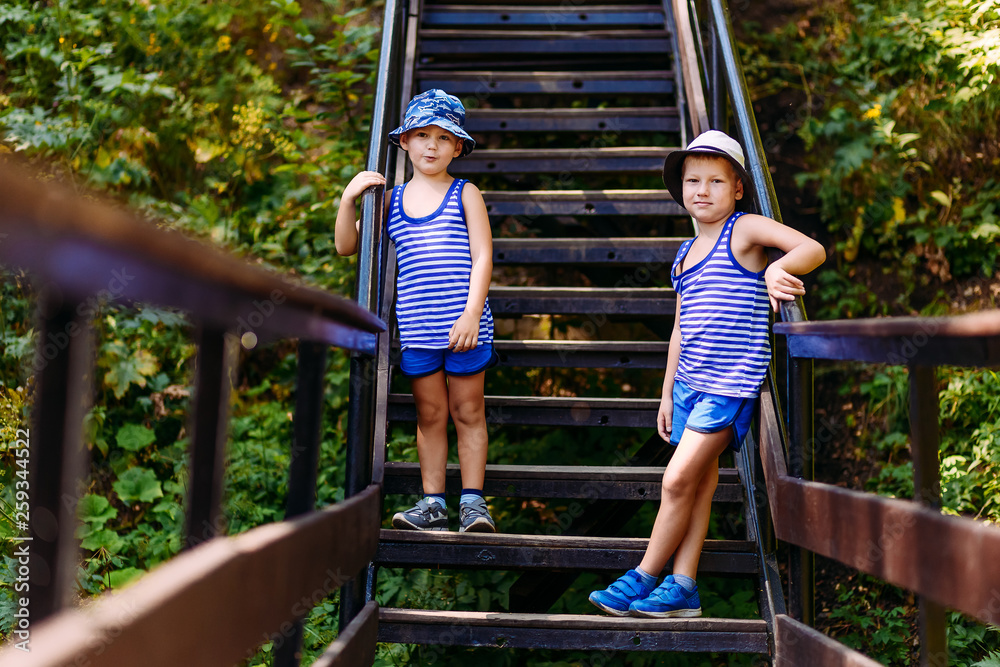 two boys in striped t-shirts and blue shorts stand on the stairs in the summer