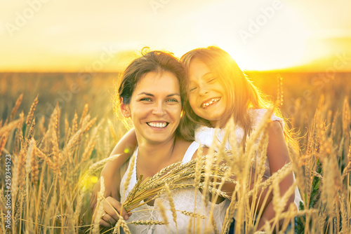 Young woman and her daughter on golden wheat field at sunny summer evening. photo