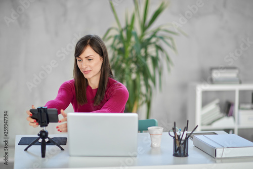 Schilderij op canvas Charming Caucasian brunette dressed casual adjusting smart phone for video call