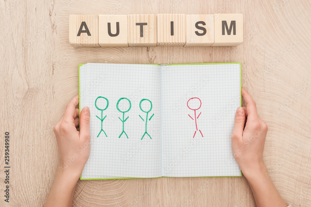 cropped view of woman holding opened notebook with drawn different humans near wooden cubes with autism lettering cropped view of woman holding opened notebook with drawn different humans near wooden cubes with autism lettering