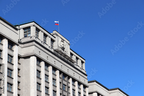 Russian flag on the Parliament building in Moscow against blue sky. Facade of State Duma of Russia with soviet coat of arms, russian authority