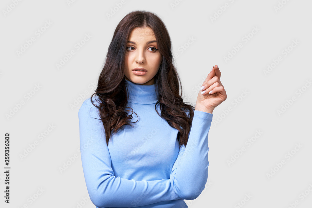 Studio image of serious young woman, wears blue long sleeve blouse, looking aside. Caucasian brunette female in blue blouse posing over white studio wall. People and emotions concept Studio image of serious young woman, wears blue long sleeve blouse, looking aside. Caucasian brunette female in blue blouse posing over white studio wall. People and emotions concept