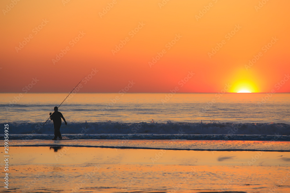 Beautiful scene with fisherman silhouette with rod sitting on sea beach at sunset