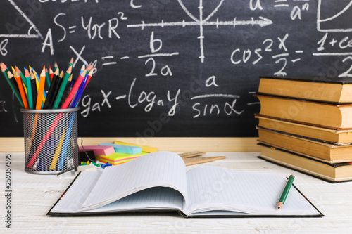 School desk in classroom, with books on background of chalk board with written formulas. Soncept Teacher's Day.