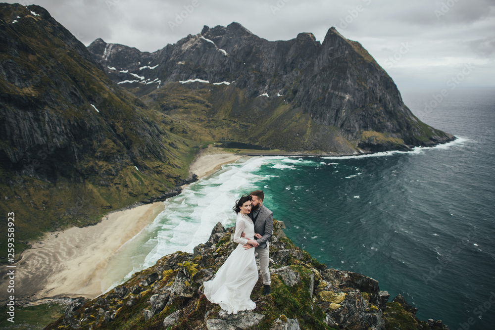 Wedding couple travelers on a hill in Norway, Kvalvika. Beautiful view of the beach, Lofoten, Norway. Wedding couple travelers on a hill in Norway, Kvalvika. Beautiful view of the beach, Lofoten, Norway.