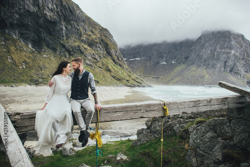 Wedding couple travelers on a hill in Norway, Kvalvika. Beautiful view of the beach, Lofoten, Norway. photo