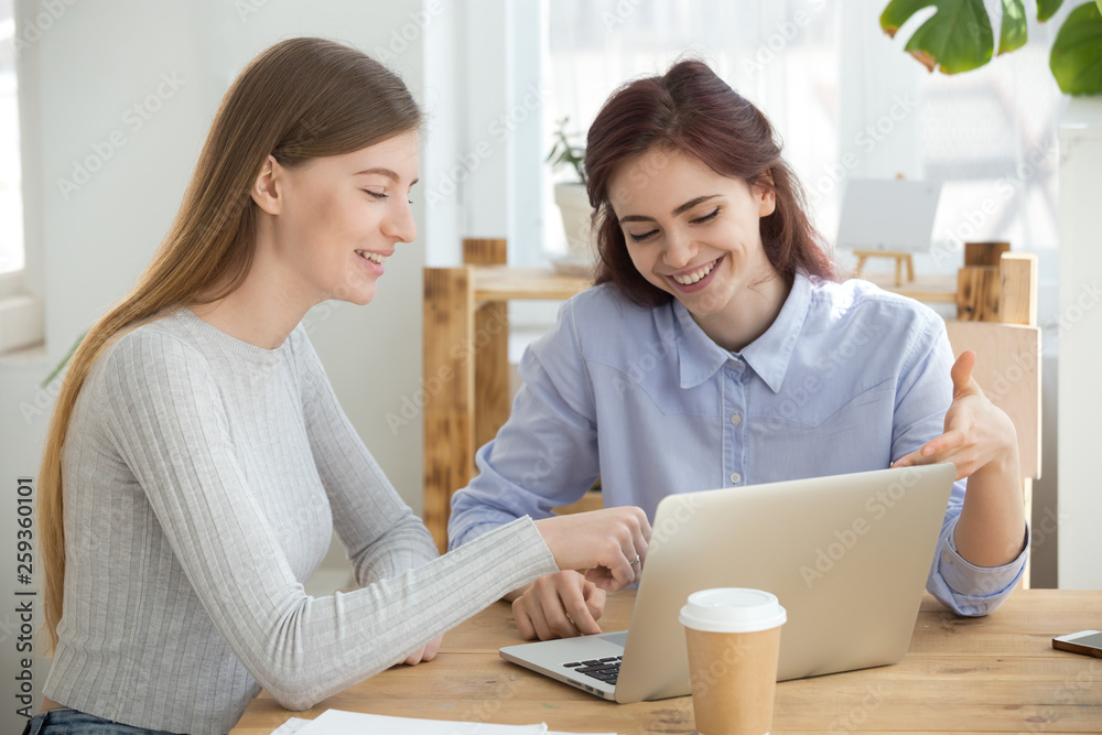 Millennial women looking at computer smiling sitting in office Millennial women looking at computer smiling sitting in office