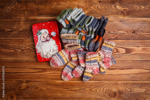multi-colored knitted baby socks and a metal box with the image of Santa Claus on a wooden background