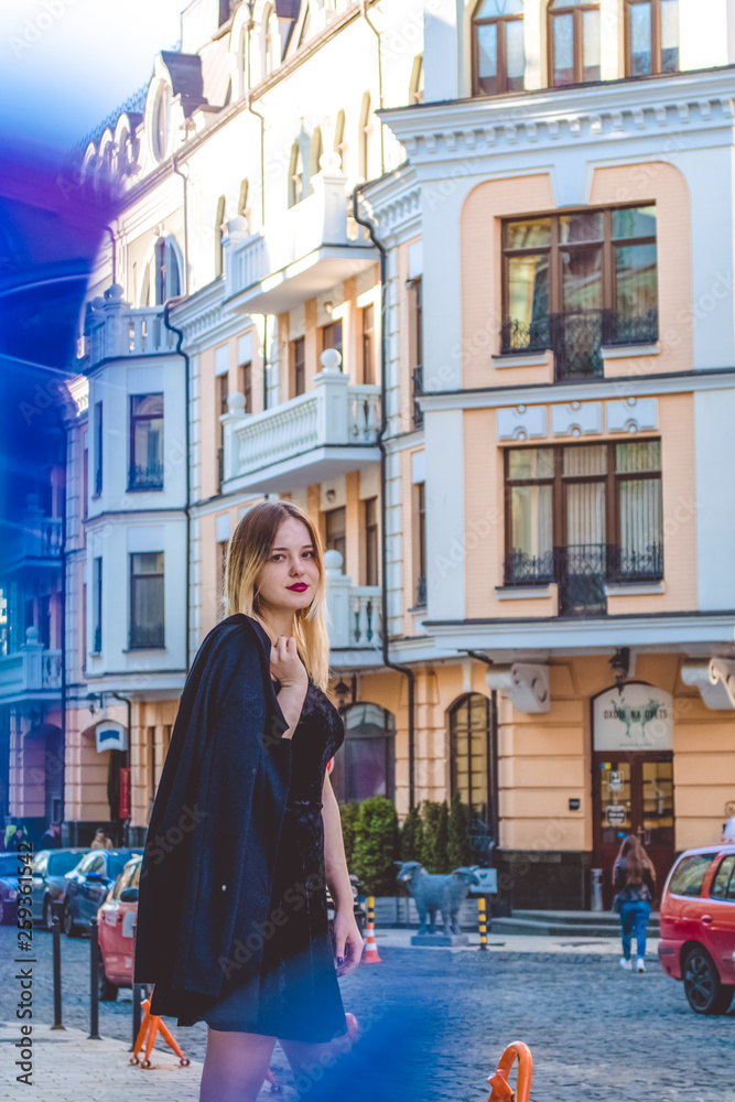 The young girl in black clothes in spring sunny day walks on old city streets. Dress and coat. Modern fashion. Patches of light. The young girl in black clothes in spring sunny day walks on old city streets. Dress and coat. Modern fashion. Patches of light.