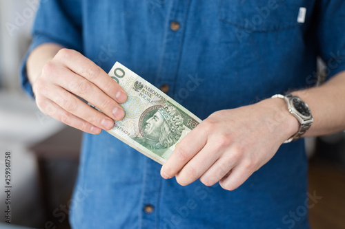 A rich young man in a casual blue shirt holding a lot of Polish money 