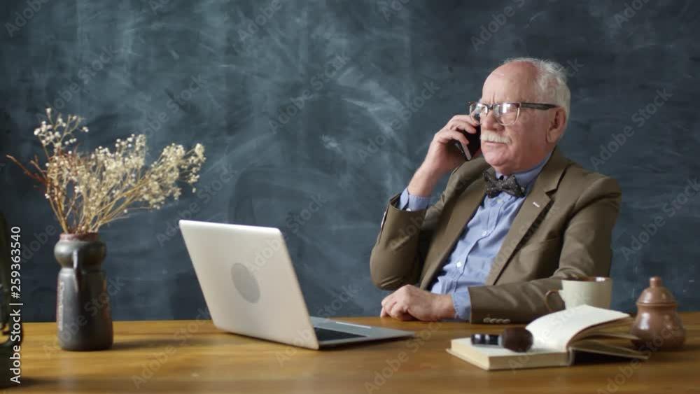 Dolly-in portrait shot of elderly man with grey hair and mustache sitting at table and talking on mobile phone Dolly-in portrait shot of elderly man with grey hair and mustache sitting at table and talking on mobile phone