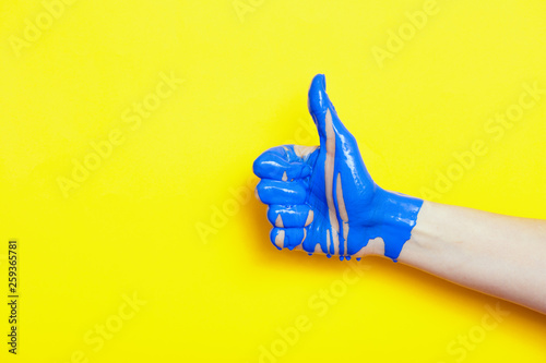 female hand showing sign thumb up with paint flowing down on a colored background. creative idea, creative concept, gesture 