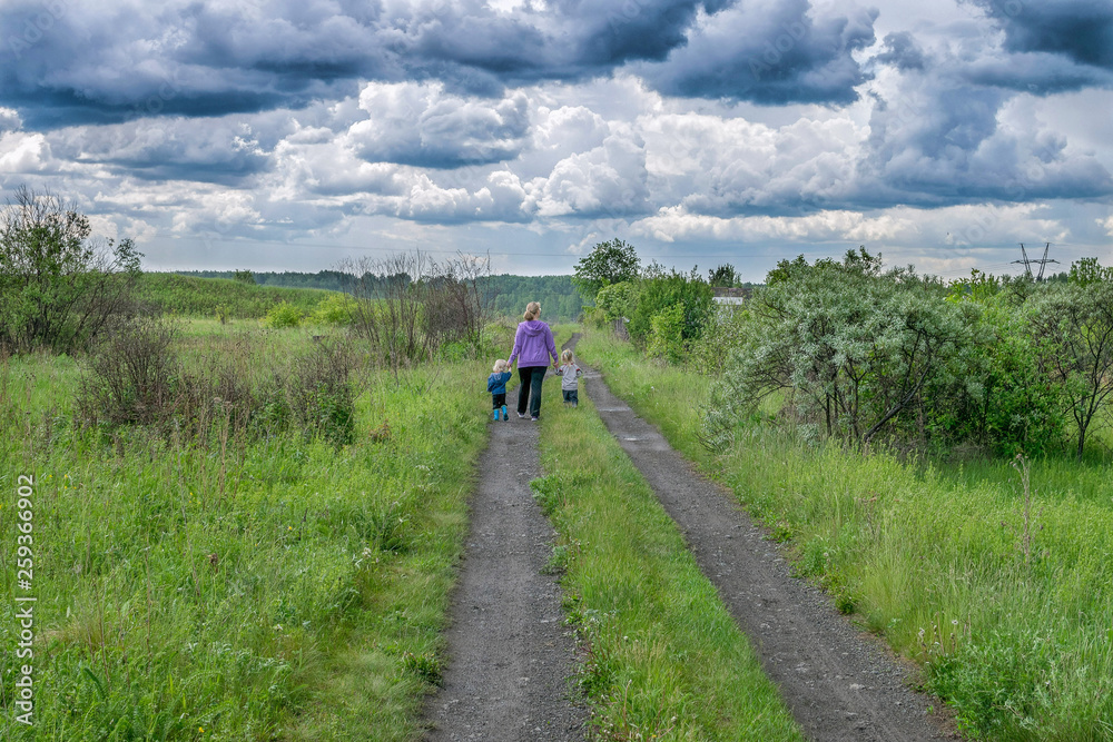 Woman and children walk on road under dark clouds