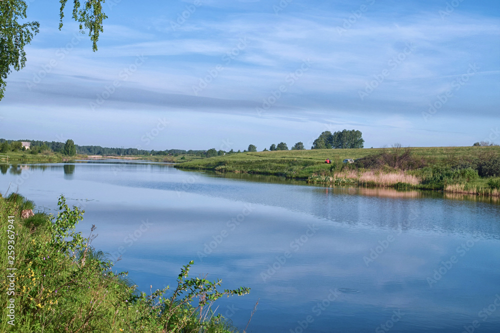 Reflection of meadow in still river at summer